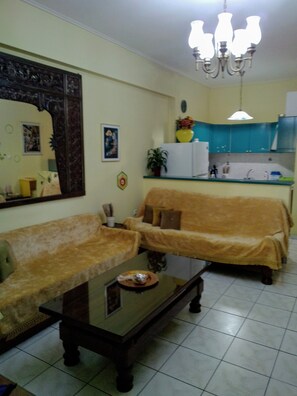 A living room with two sofas, a coffee table, a large mirror, and a kitchen area with a refrigerator and sink. - Palinas comfy home!! (Kalamata)