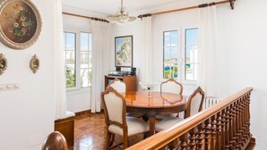 A dining area with a wooden table, chairs, a chandelier, and a view of the outdoors through large windows.
