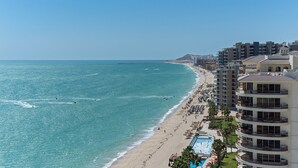 Un hôtel situé sur la côte, avec vue sur la plage, de nombreux balcons et une piscine.
