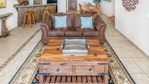 Ein Wohnzimmer mit braunem Ledersofa, zwei gemusterten Kissen, einem Couchtisch aus Holz mit einer Dekorschale und einem gemusterten Teppich.