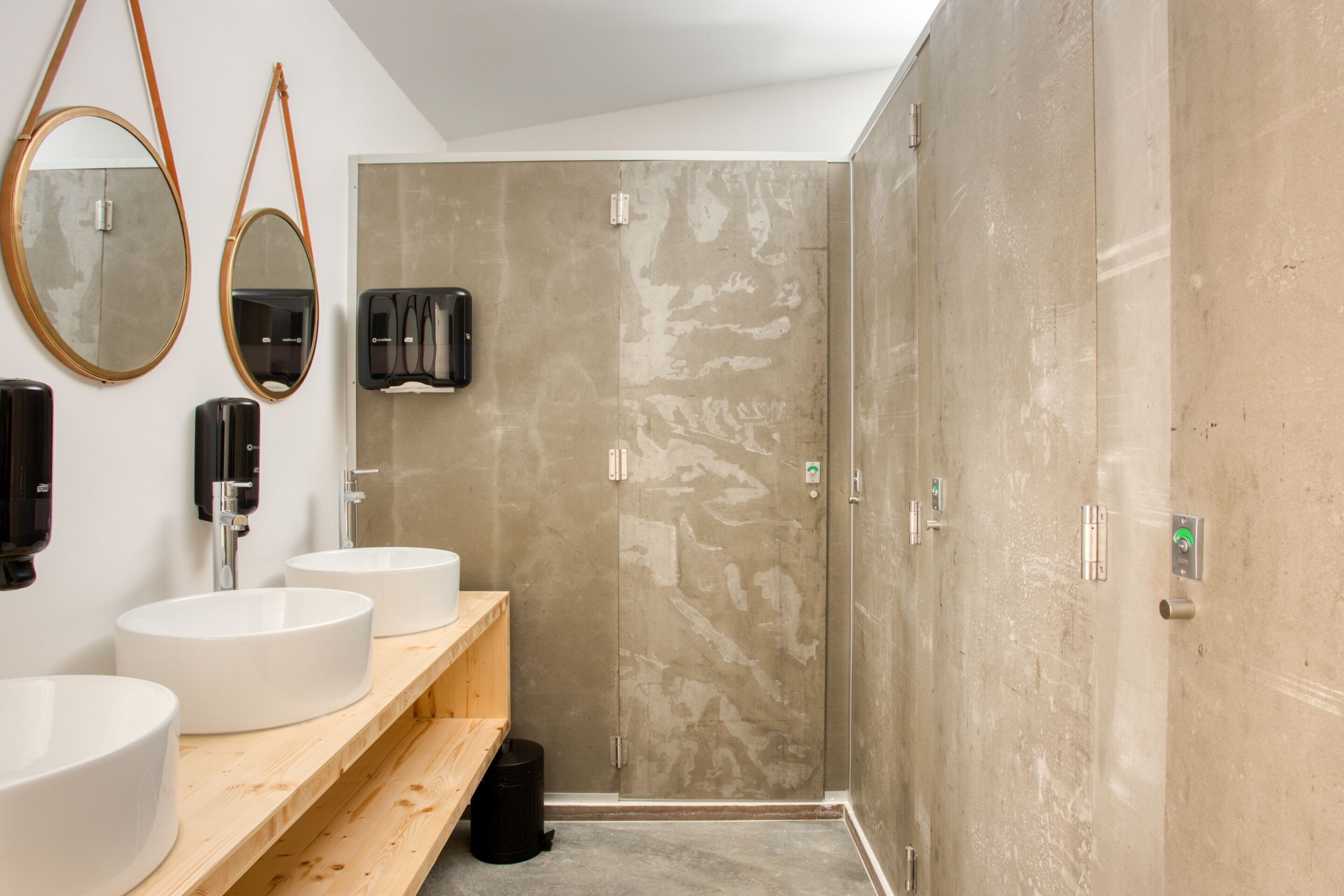 A bathroom with two sinks, a mirror, a towel dispenser, and a shower area.