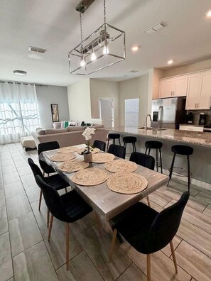 A modern kitchen with a dining area, featuring a large island, stainless steel appliances, and a contemporary light fixture.