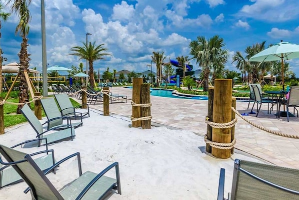 A poolside area with lounge chairs, a pool, palm trees, and a clear sky.