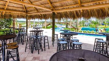 An outdoor patio area with tables and stools, a pool, and a view of a tropical landscape.