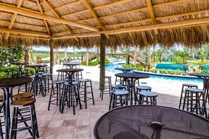 Un área de patio al aire libre con mesas y taburetes, una piscina y vistas a un paisaje tropical.