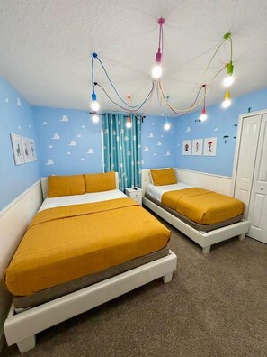 A bedroom with two beds, a white wardrobe, and a ceiling with colorful hanging lights.