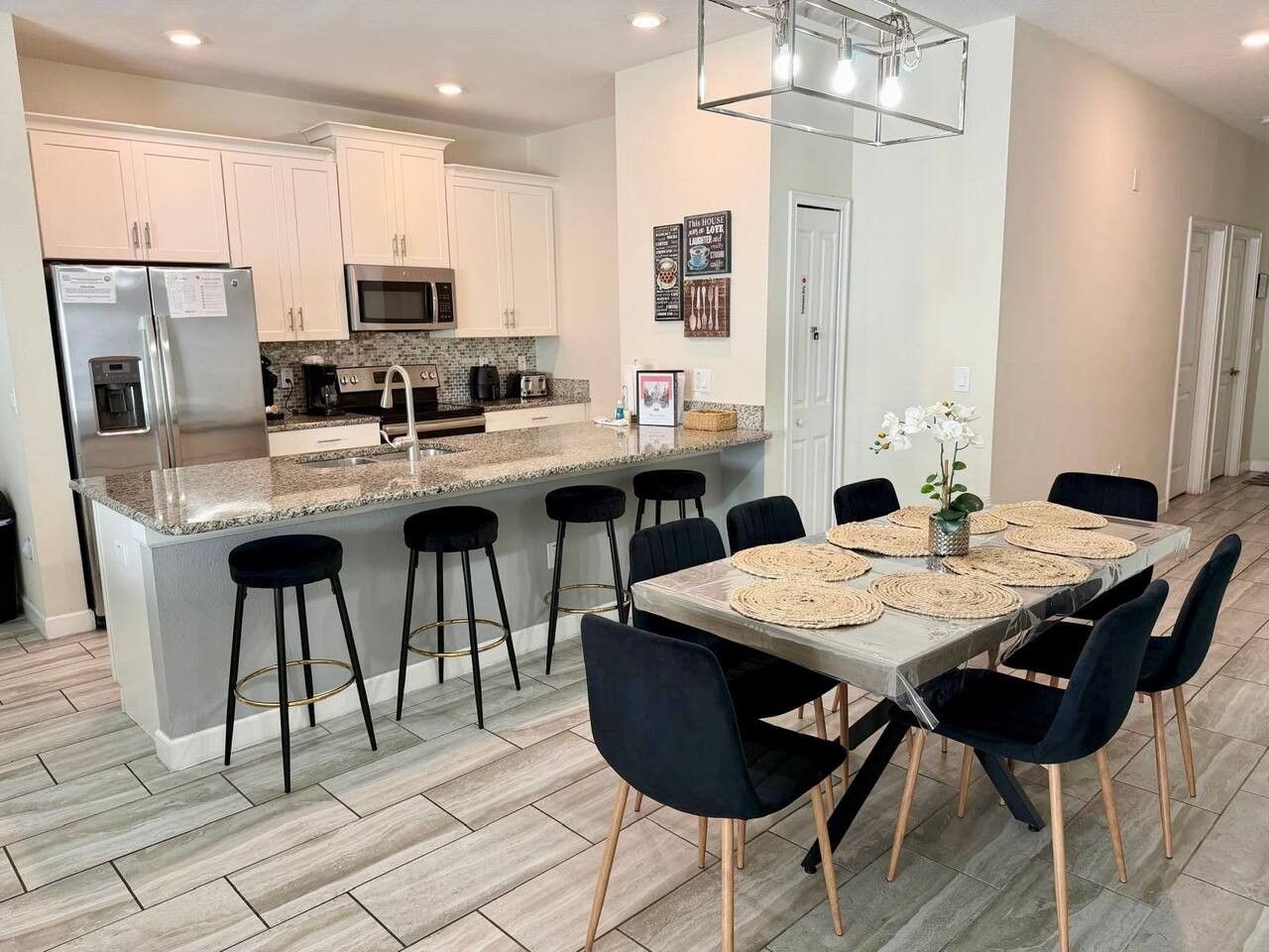 A modern kitchen with a central island, bar stools, and a dining table set for six.
