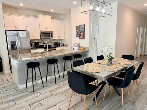 A modern kitchen with a central island, bar stools, and a dining table set for six. - Resort/Private Pool! Near Disney!Sleeps13 (Kissimmee)