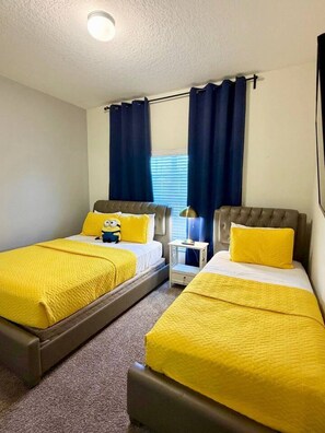 A room with two beds, each with a yellow bedspread and pillows, a small bedside table with a lamp, and a window with blue curtains. - Resort/Private Pool! Near Disney!Sleeps13 (Kissimmee)