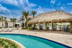 A swimming pool with a thatched roof structure, lounge chairs, and a poolside area with tables and chairs. - Resort/Private Pool! Near Disney!Sleeps13 (Kissimmee)