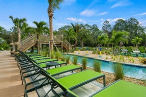 Un área junto a la piscina con sillones de descanso y un pequeño puente.
