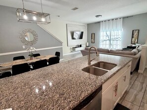 Una cocina moderna con encimeras de granito, un lavamanos doble y un comedor con mesa y sillas.