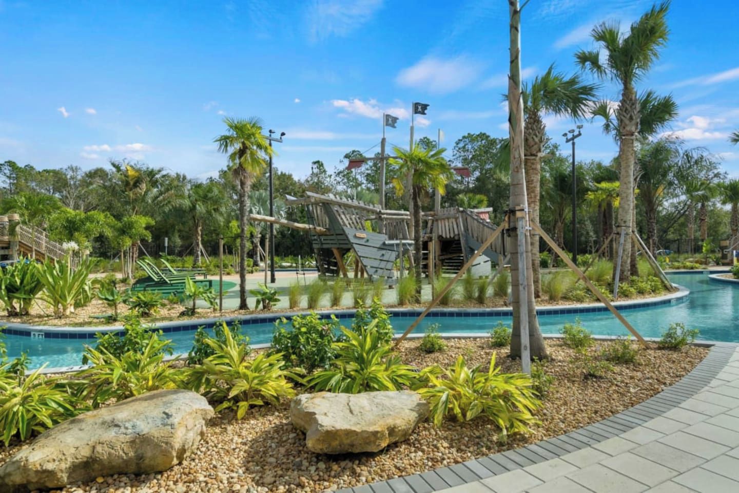 A pool area with palm trees, a wooden bridge, and a clear sky.