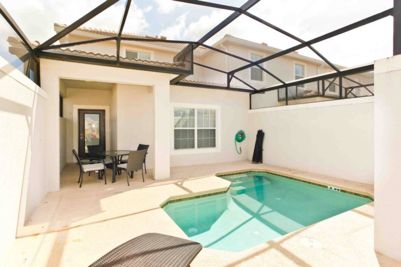 Una piscina exterior techada con un patio, una mesa y sillas, y una ventana.