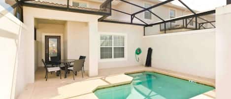 Una piscina exterior techada con un patio, una mesa y sillas, y una ventana.