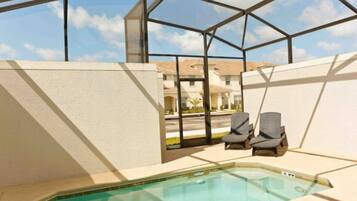 A pool area with a glass enclosure, two lounge chairs, and a view of a residential street.
