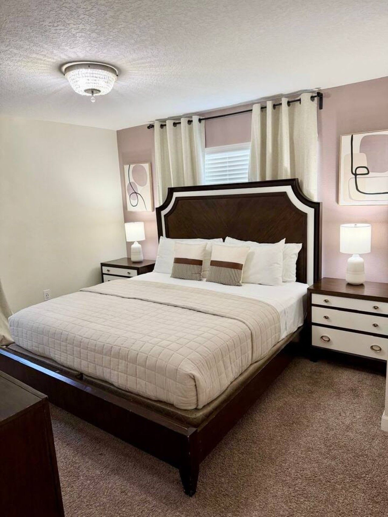 A bedroom with a large bed, a nightstand with a lamp, a dresser, and a ceiling light fixture.