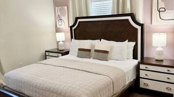 A bedroom with a large bed, a nightstand with a lamp, a dresser, and a ceiling light fixture.