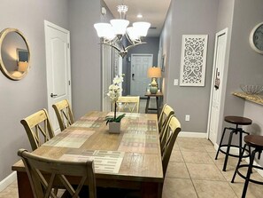 Enjoy meals in this elegant dining area with a long table and six chairs, surrounded by decorative wall art and a chandelier.
