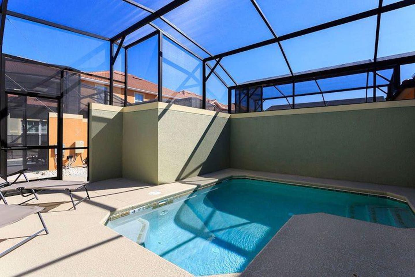 Una piscina con un recinto in vetro, circondata da un patio con sedie.