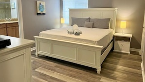 A bedroom with a large bed, bedside tables, a nightstand, a dresser, a window with blinds, and a painting on the wall. - Resort Home Sleeps 12 w/private Pool! (Kissimmee)