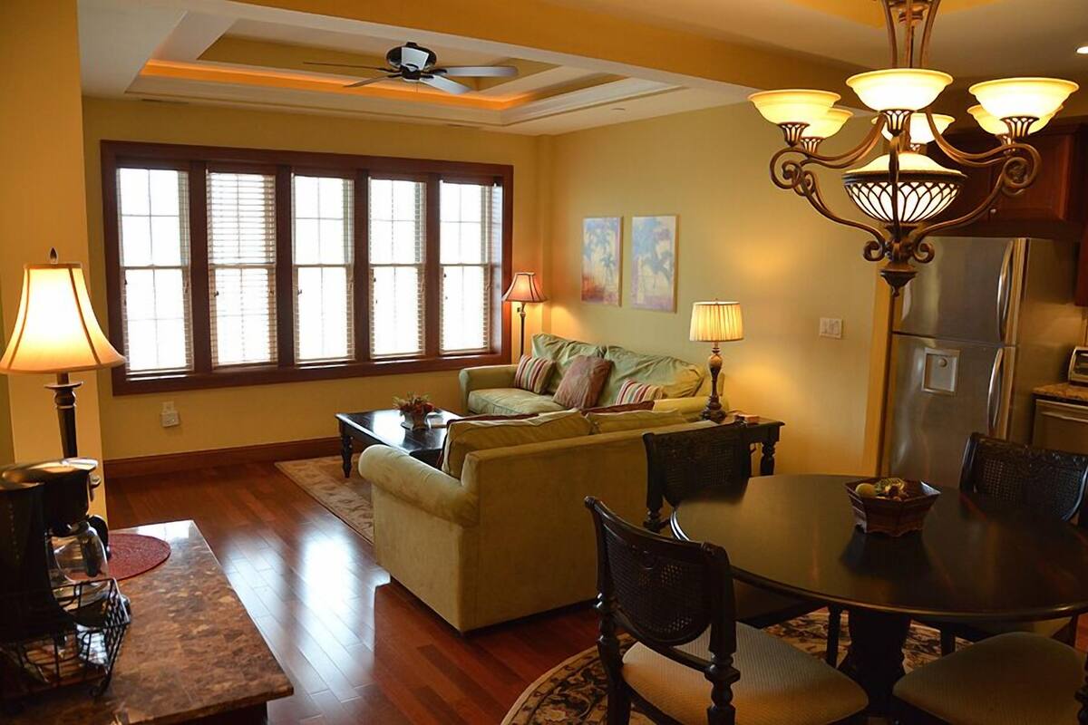 A living room with a sofa, dining table, chairs, a coffee table, a fireplace, and a large window with blinds.