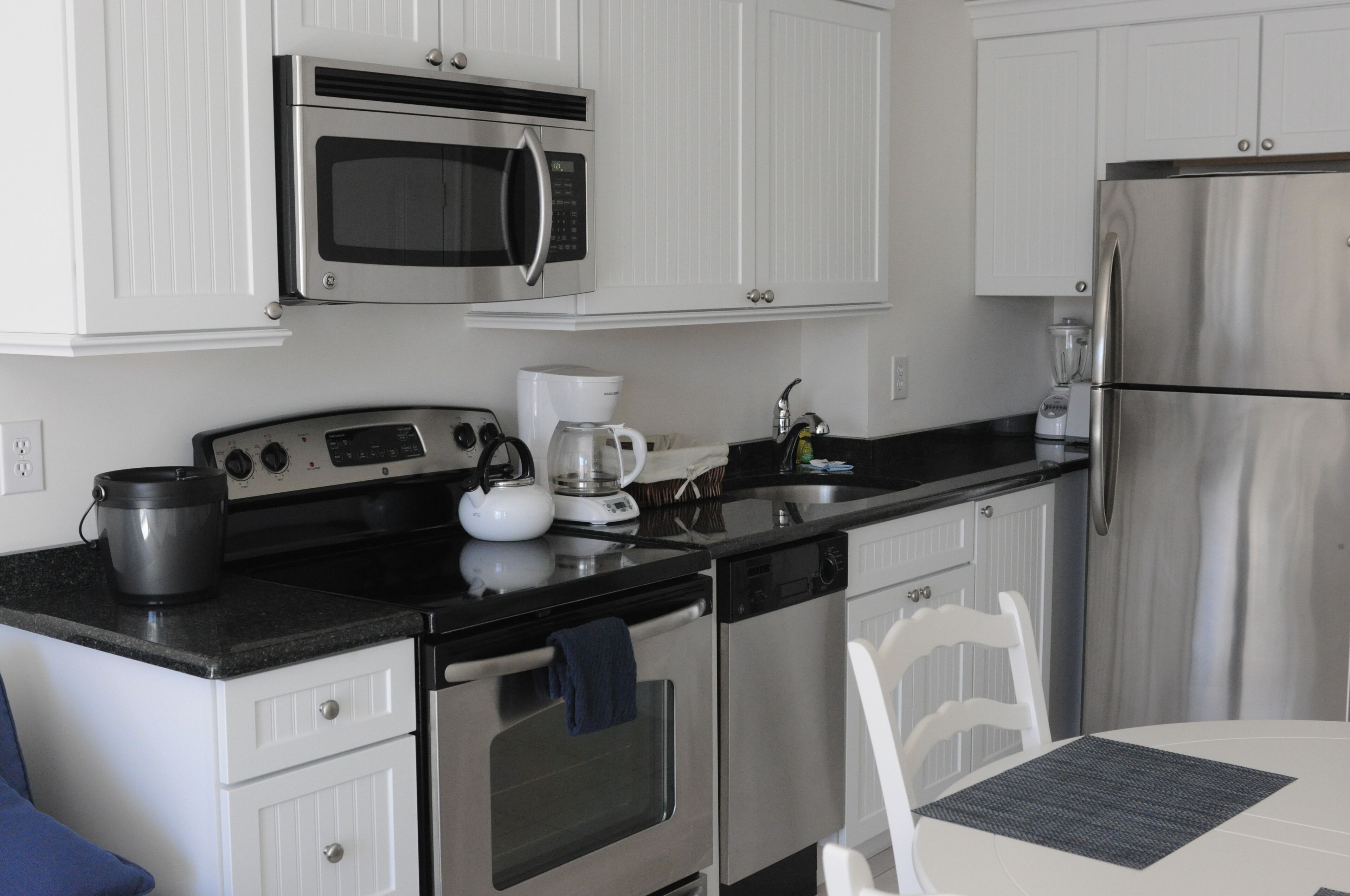 A modern kitchen with white cabinetry, stainless steel appliances including a microwave, stove, and refrigerator, a coffee maker, and a dishwasher.