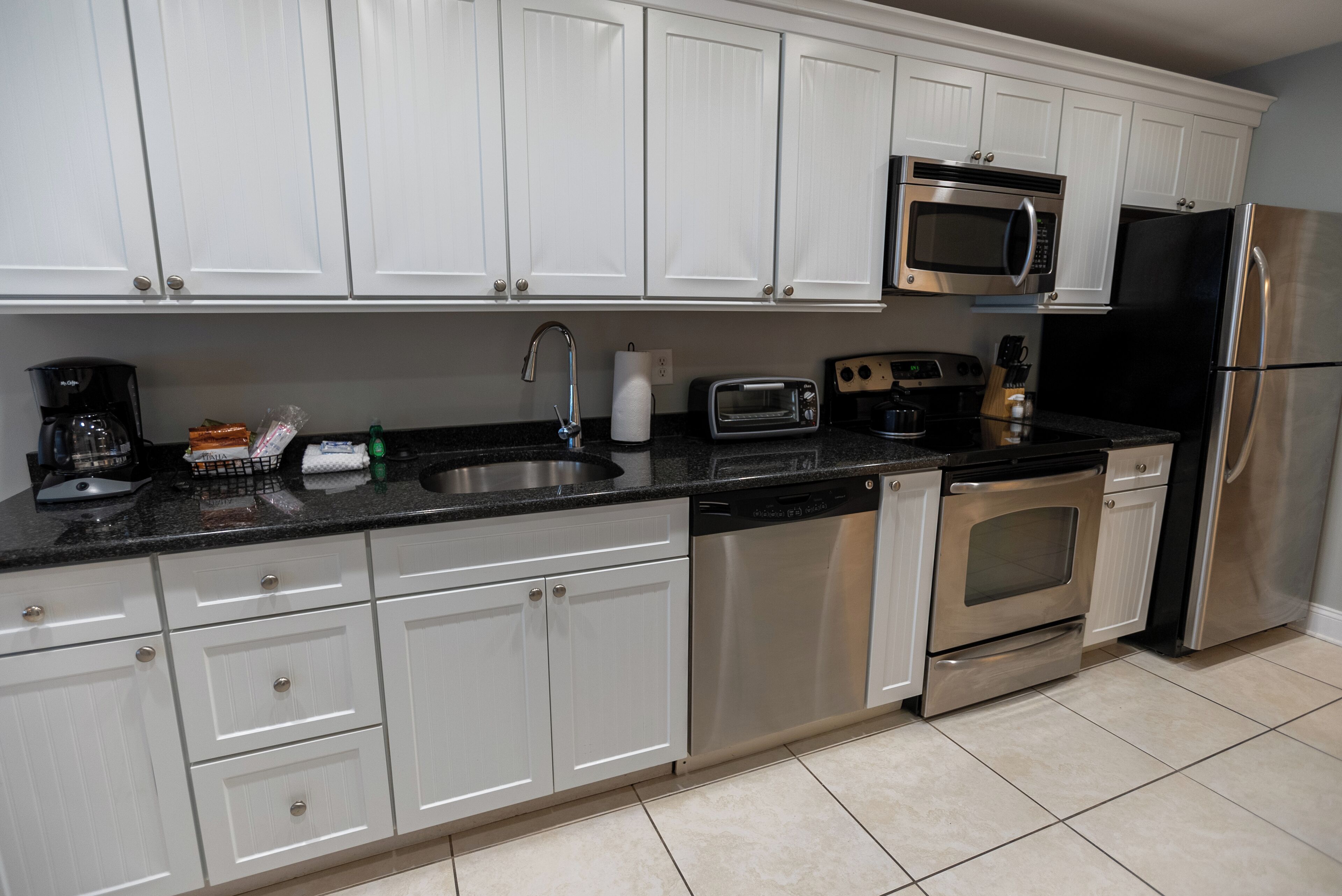 A modern kitchen with white cabinets, stainless steel appliances including a microwave, oven, and refrigerator, a dishwasher, and a granite countertop.