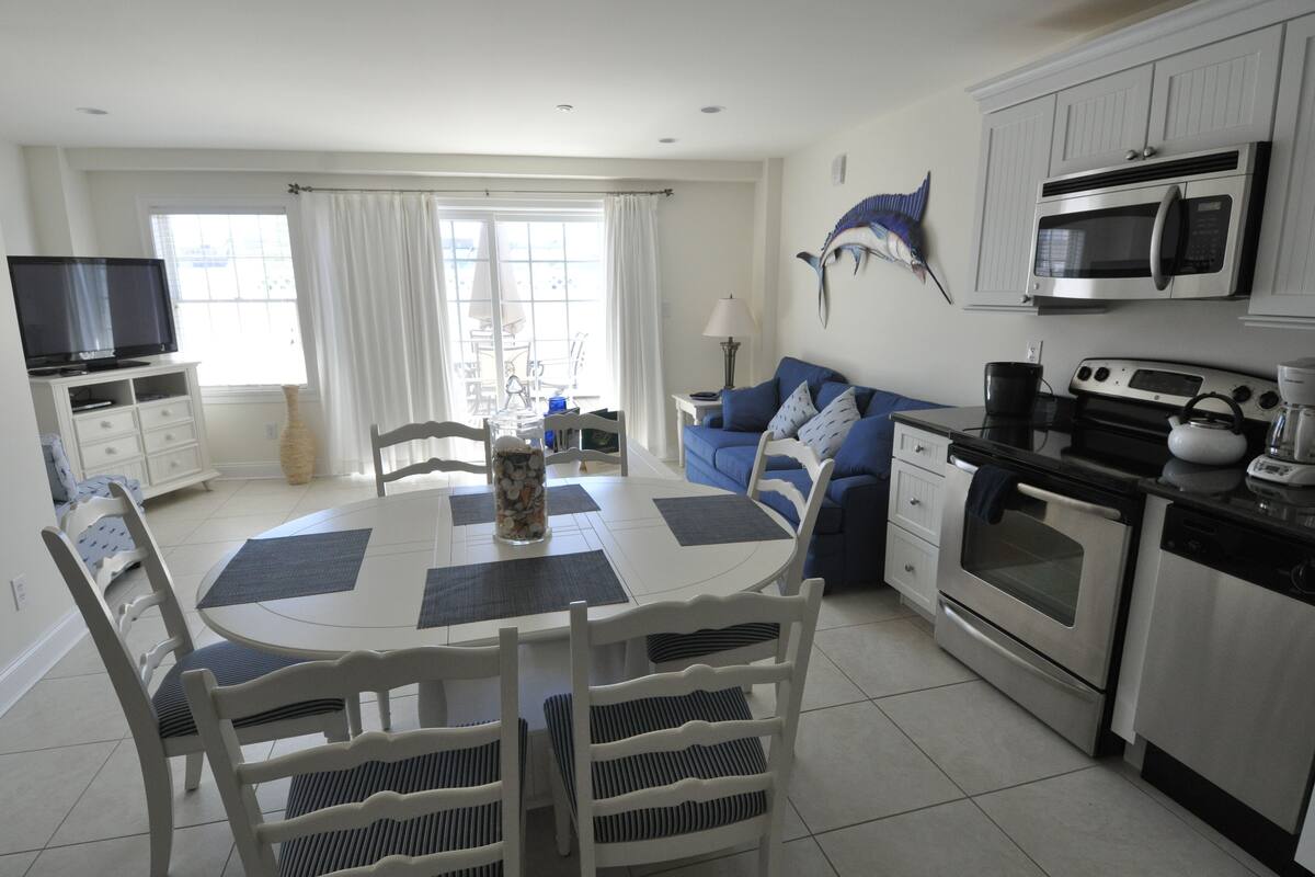 A modern kitchen with white cabinetry, a dining area with a round table and chairs, and a blue sofa.