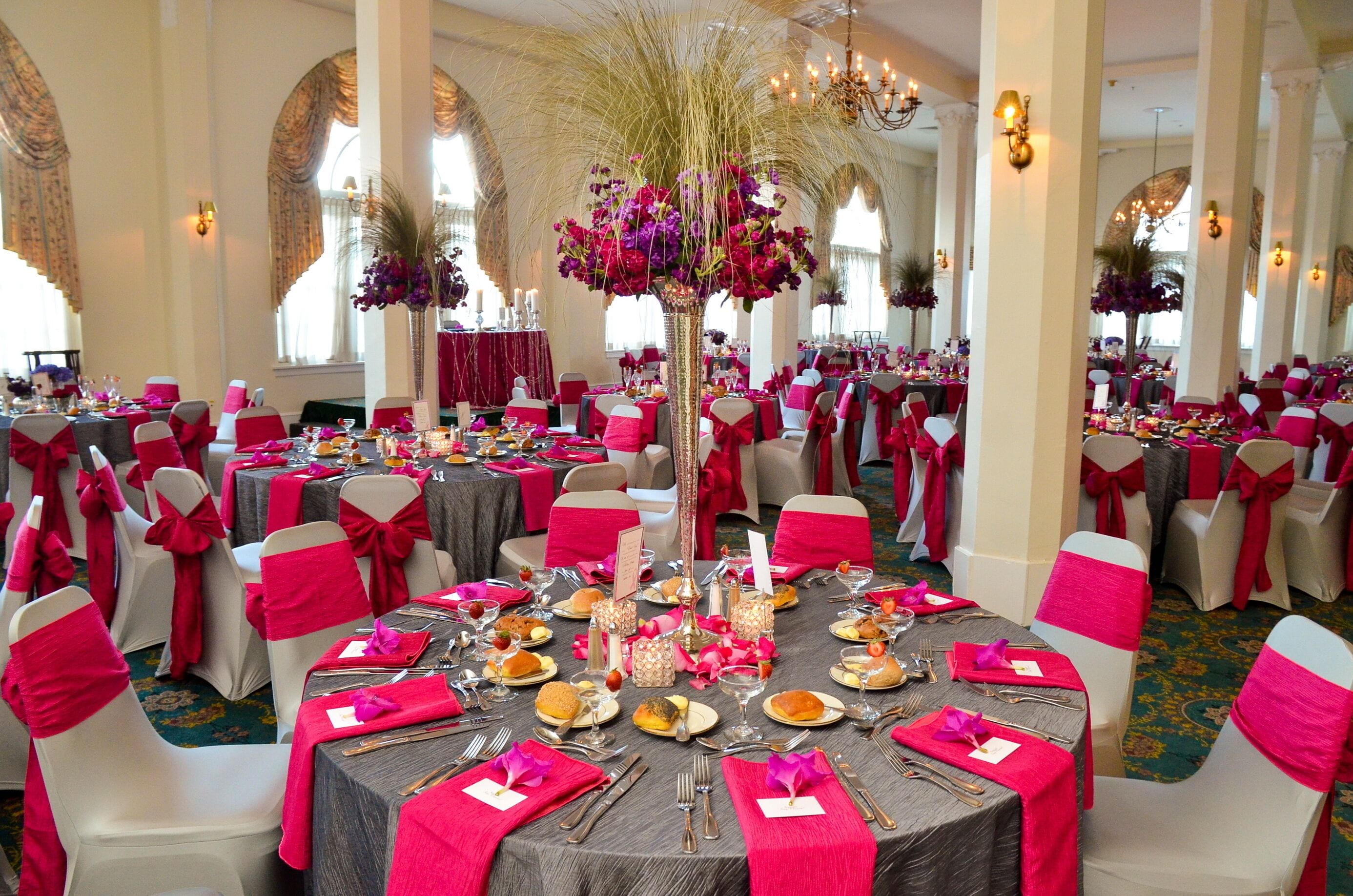 A banquet hall with round tables, red and white chairs, and floral centerpieces.