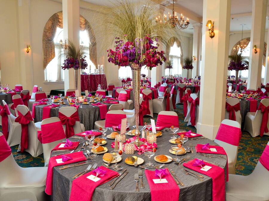 A banquet hall with round tables, red and white chairs, and floral centerpieces.