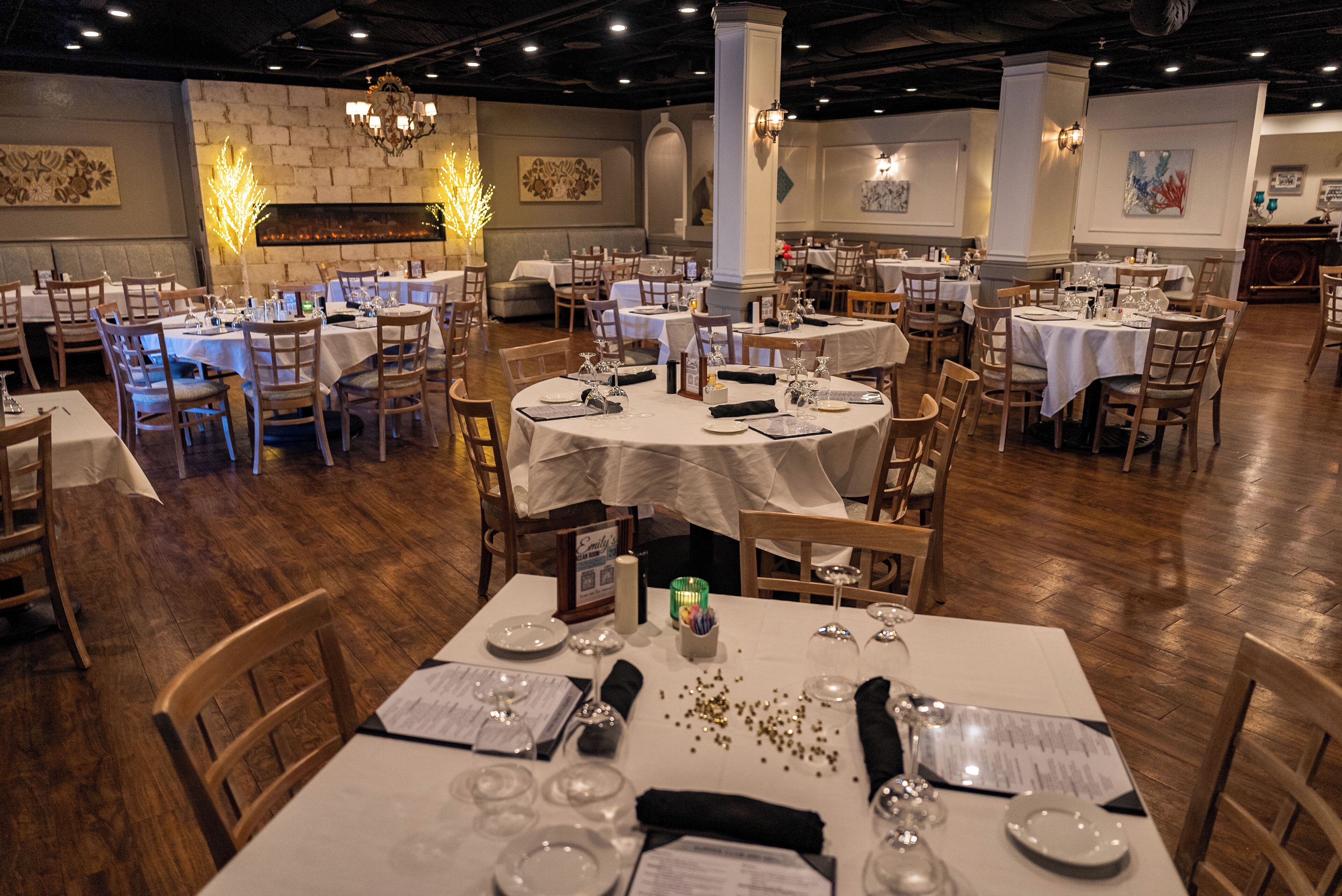 Een restaurant met meerdere ronde tafels gedekt voor diners, houten stoelen en een kroonluchter.