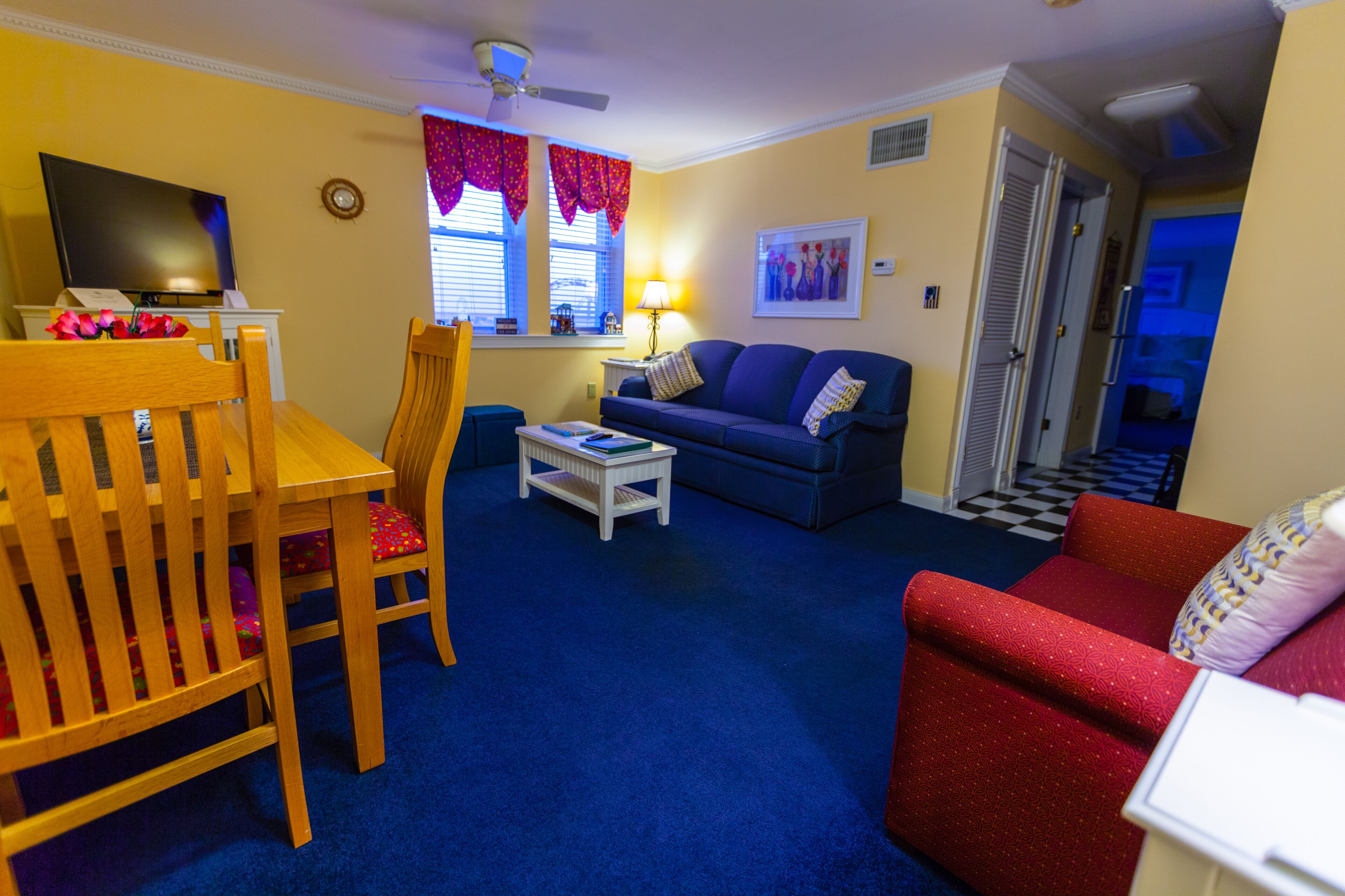 A living room with a blue carpet, wooden furniture, a television, and a red couch.