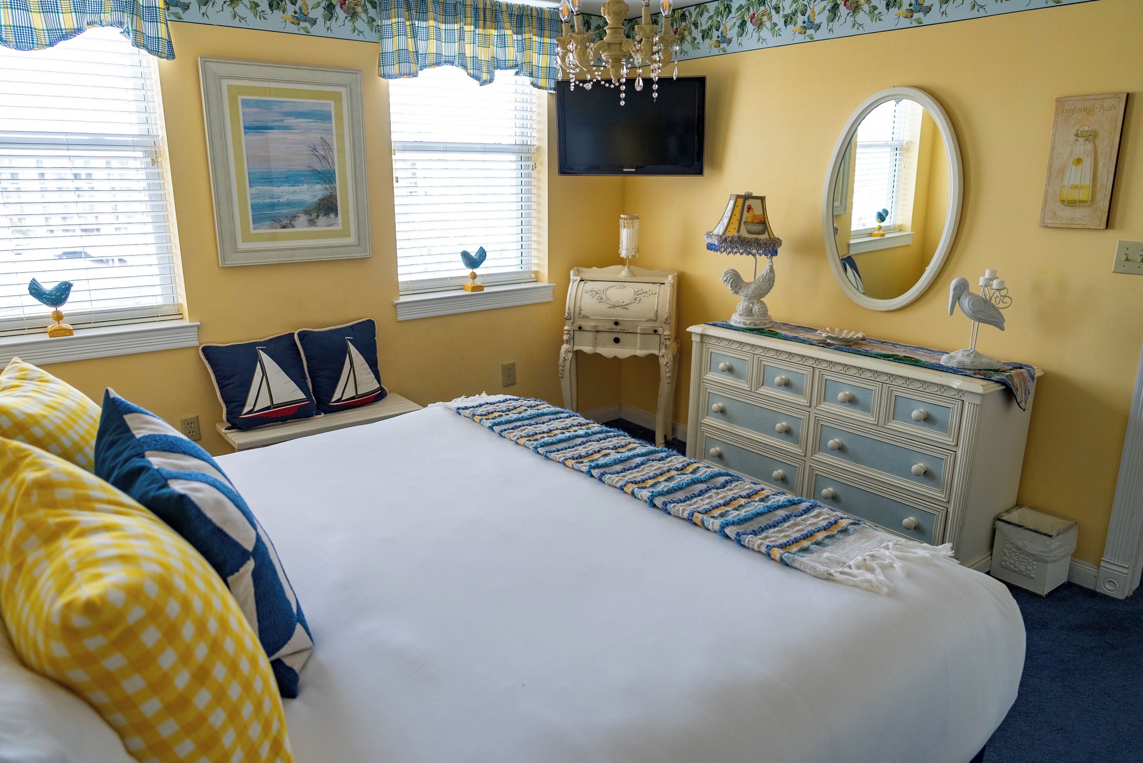A neatly arranged bedroom with a large bed, a dresser, a television, and a window with blinds.