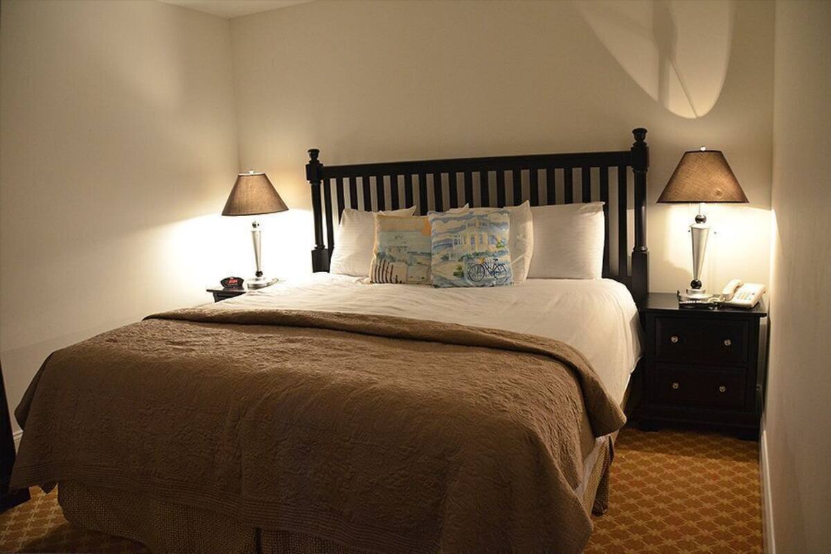 A neatly made bed with a brown blanket, two bedside tables with lamps, and a nightstand with a telephone.