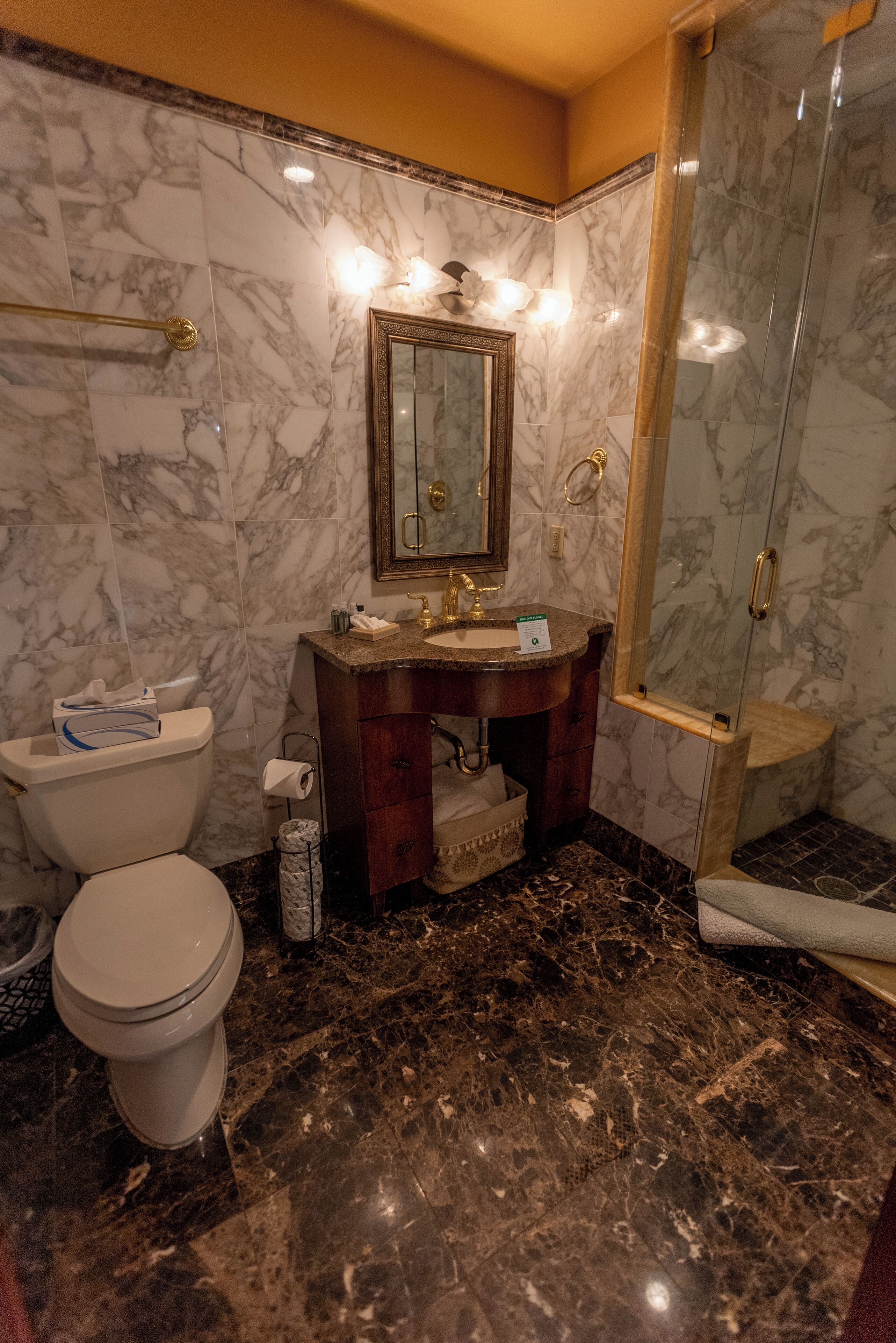 Une salle de bain avec des murs en marbre, un lavabo avec un miroir, des toilettes et une douche à parois de verre.