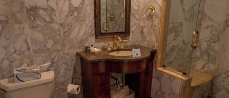 Un baño con paredes de mármol, un lavabo con espejo, inodoro y cabina de ducha con mampara de vidrio.