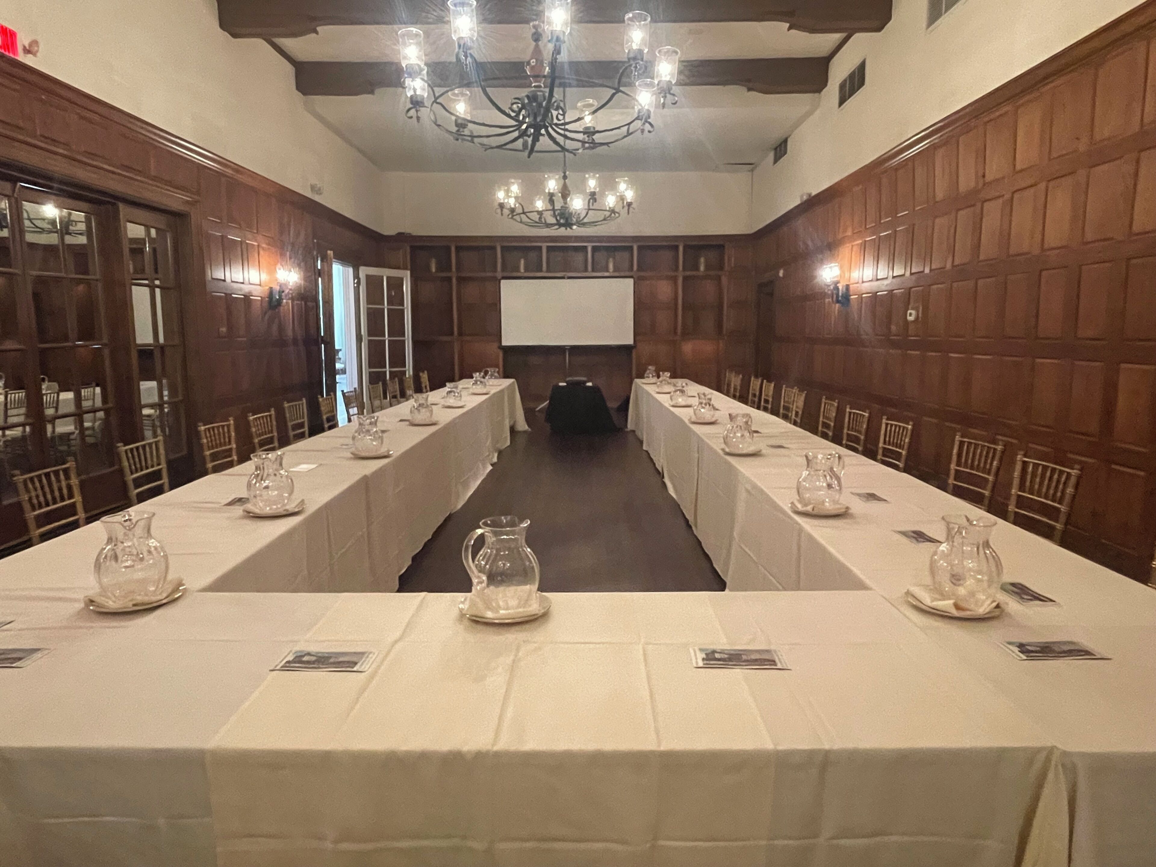 Une salle de conférence avec une longue table préparée pour une réunion, des murs lambrés et un lustre.
