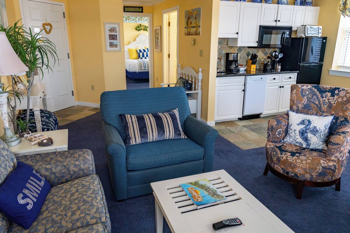 A living room with a blue sofa, patterned armchair, and a coffee table with a remote control.
