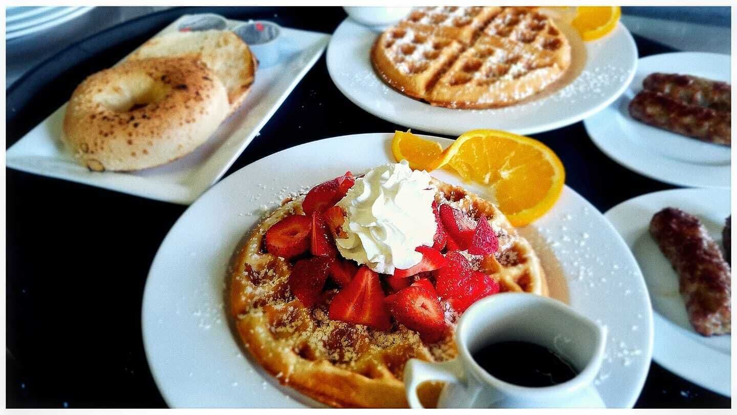 A breakfast setting with waffles, a bagel, and a plate with strawberries and whipped cream.