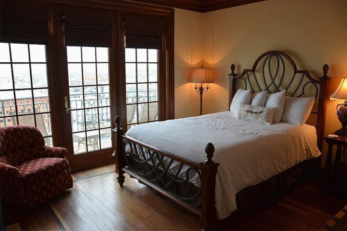 A bedroom with a large bed, two bedside lamps, a chair, and a view through a window.