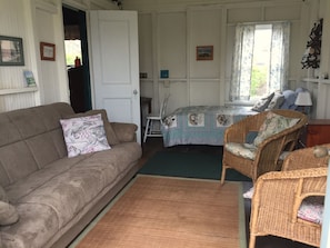 Une pièce chaleureuse avec un canapé marron, un fauteuil en osier, une petite table et un lit recouvert d’une literie à motifs floraux.