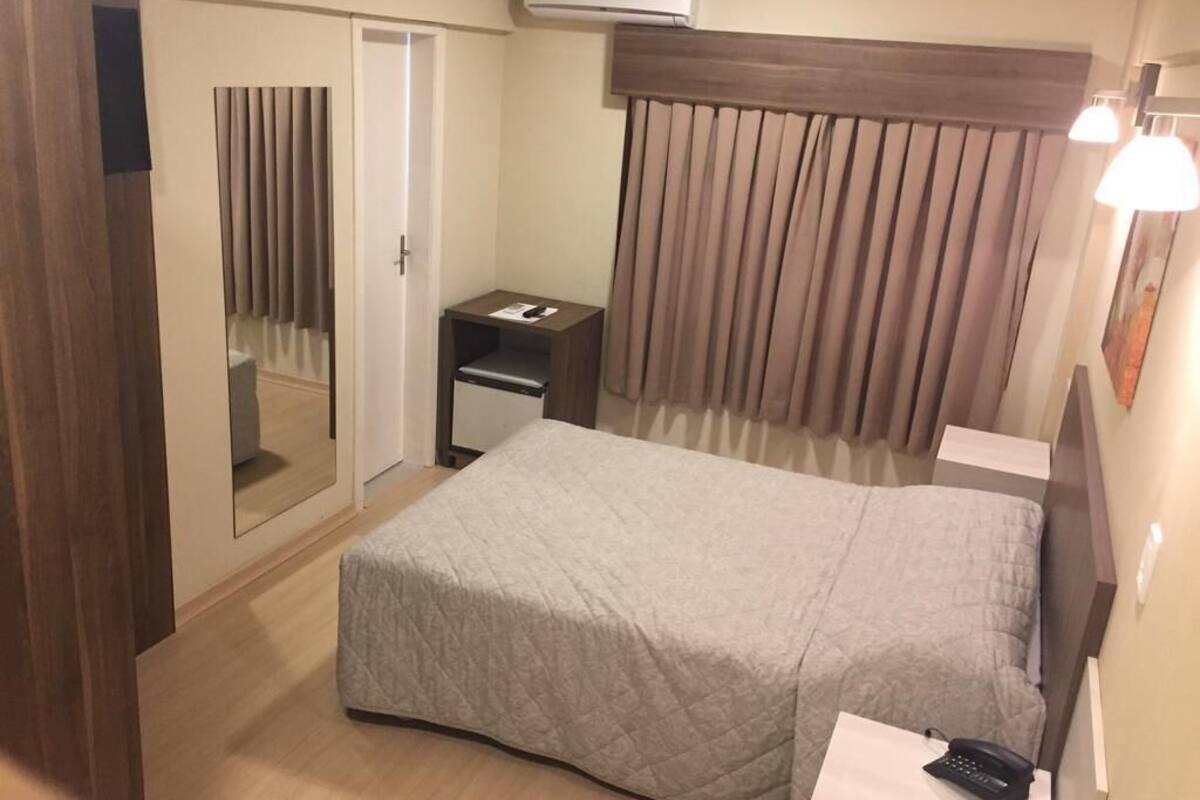 Ein Hotelzimmer mit Bett, Nachttisch mit Lampe, Spiegel, Kleiderschrank und Klimaanlage.