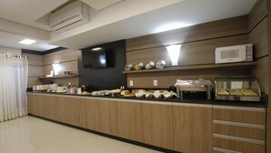 A modern kitchen with wooden cabinets, a microwave, and a buffet counter with various food items. - Hotel Klein Vllle Plus (Dois Irmaos)
