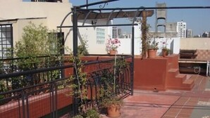 Terraço no telhado com plantas em vasos, pérgola e vista para o horizonte da cidade.