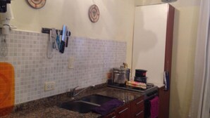 Uma cozinha com bancada de granito, pia e fogão. Há dois pratos pendurados na parede e um par de tesouras no balcão.