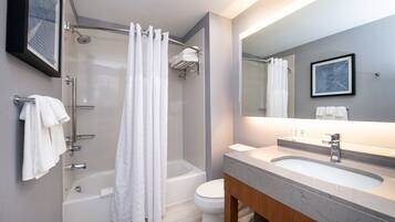 Un baño moderno con ducha envuelta en vidrio, bañera y tocador con lavamanos y espejo.