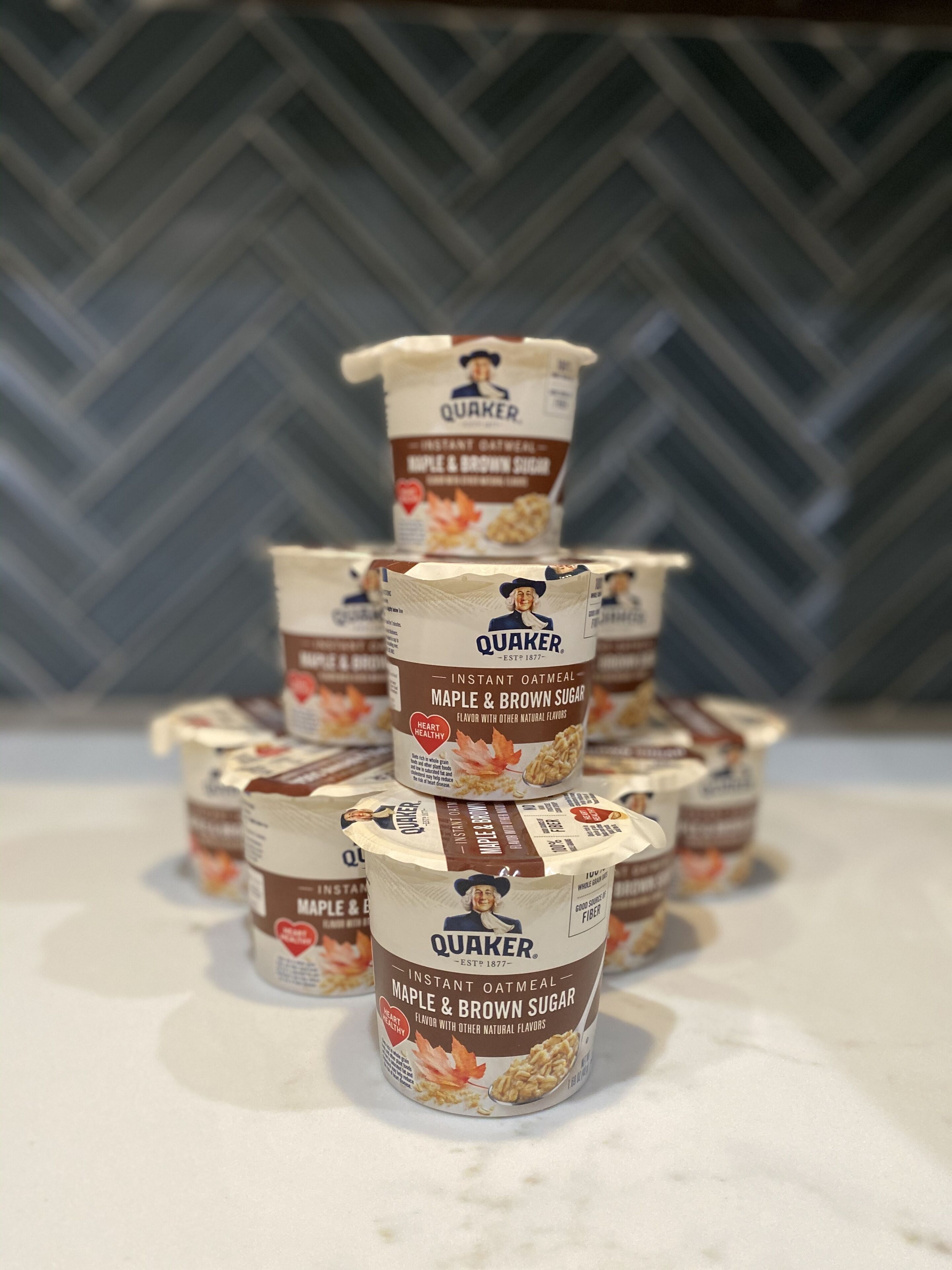 A stack of Quaker instant oatmeal containers in maple and brown sugar flavor.