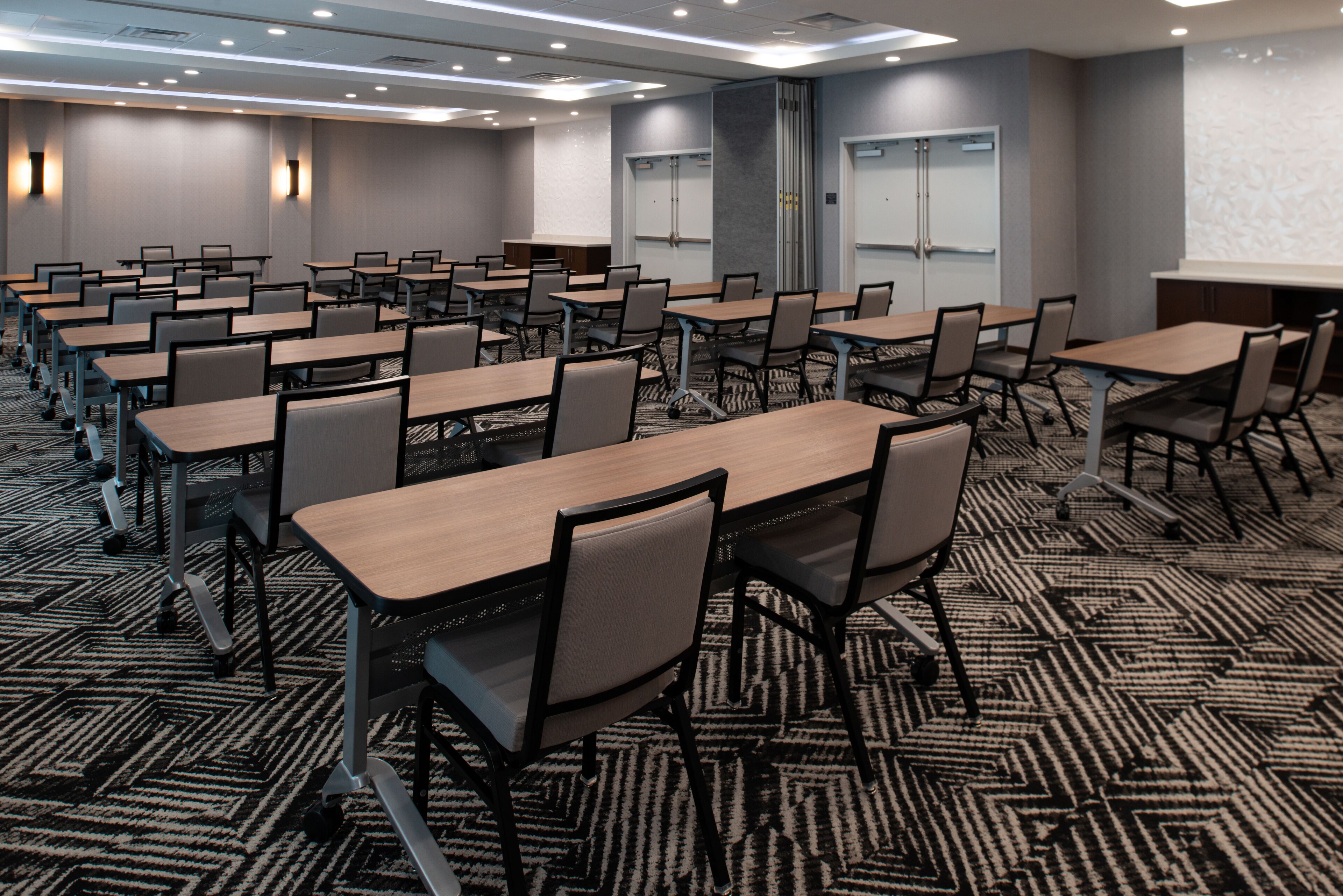 A conference room with multiple tables and chairs, carpeted floor, and a projector screen on the wall.