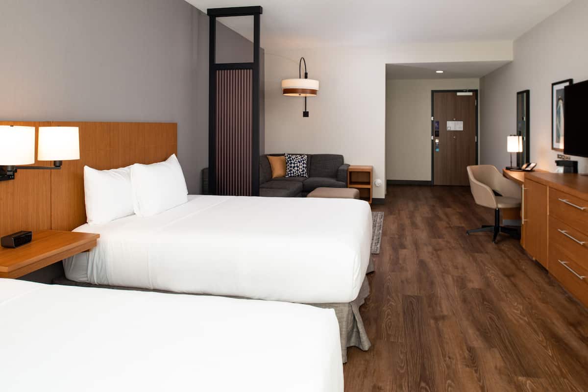 A hotel room with two beds, a desk, a chair, a TV, and a lamp.